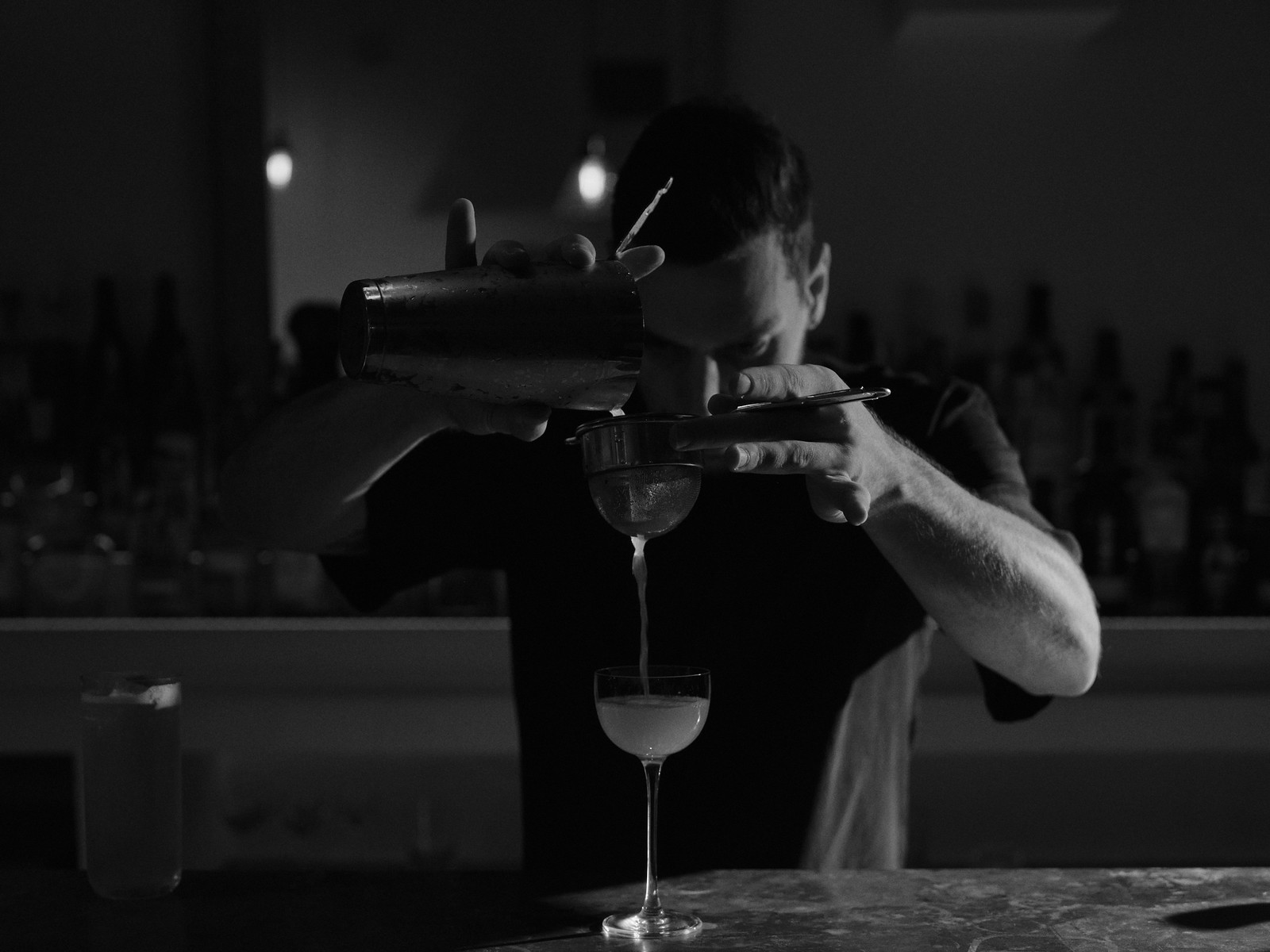 A bartender pouring a cocktail through a strainer